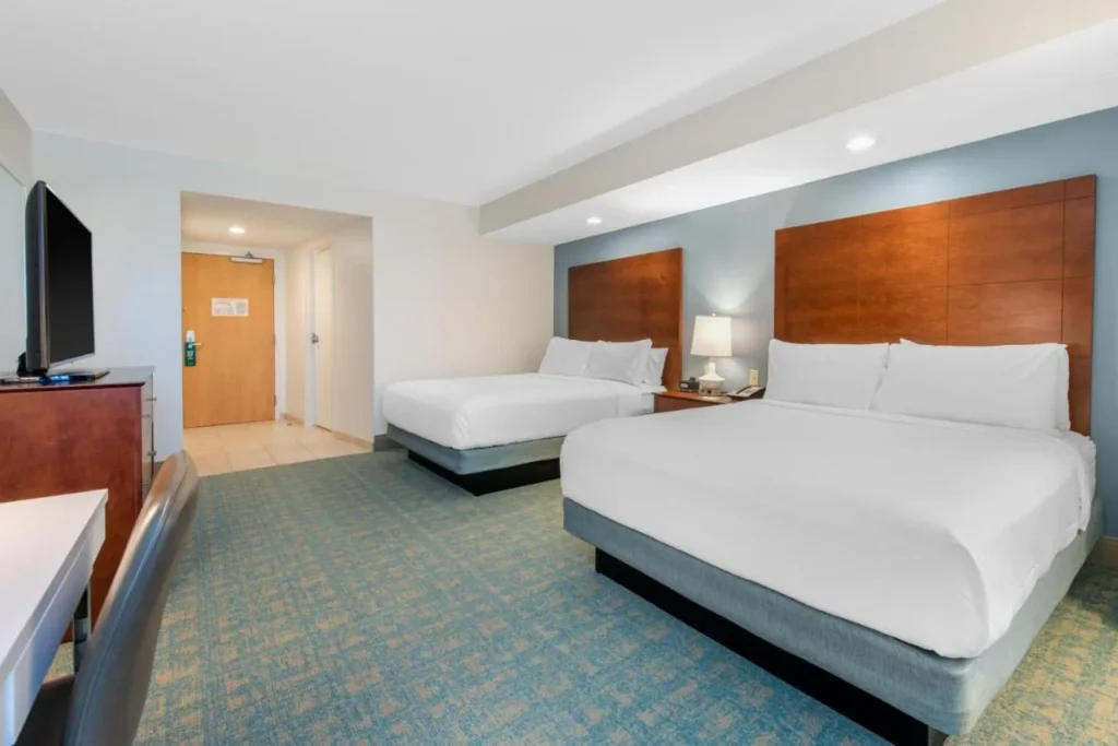 Two-queen guest room with wood headboards and blue-green carpet at Holiday Inn Orlando Disney Springs Area