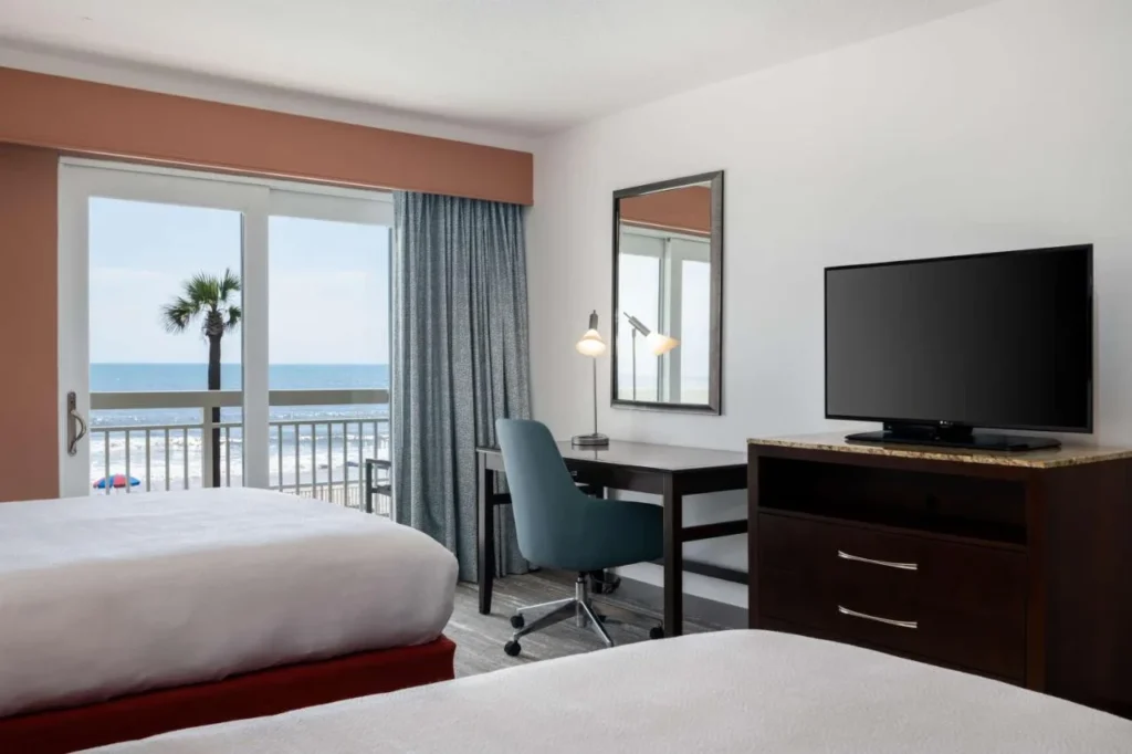 Two-queen room with a desk and balcony overlooking the beach at Hilton Garden Inn Daytona Beach Oceanfront