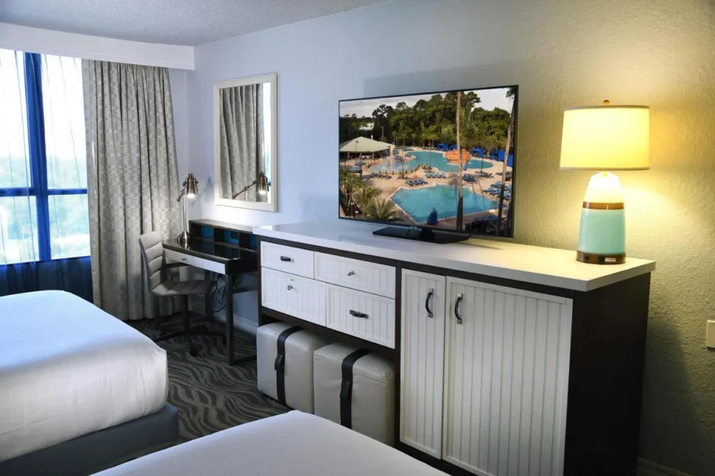 Two-queen room with a desk, dresser and TV showing the pool at Wyndham Lake Buena Vista