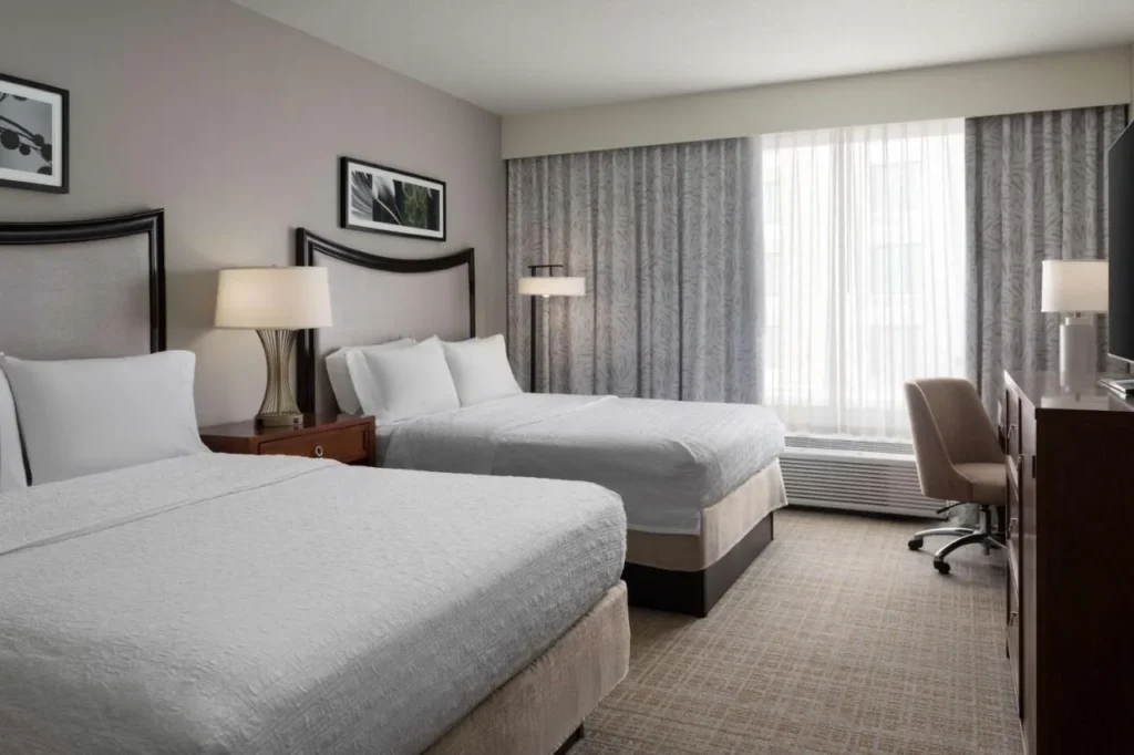 Two-queen room with desk chair and sheer curtains at Hampton Inn & Suites Downtown South
