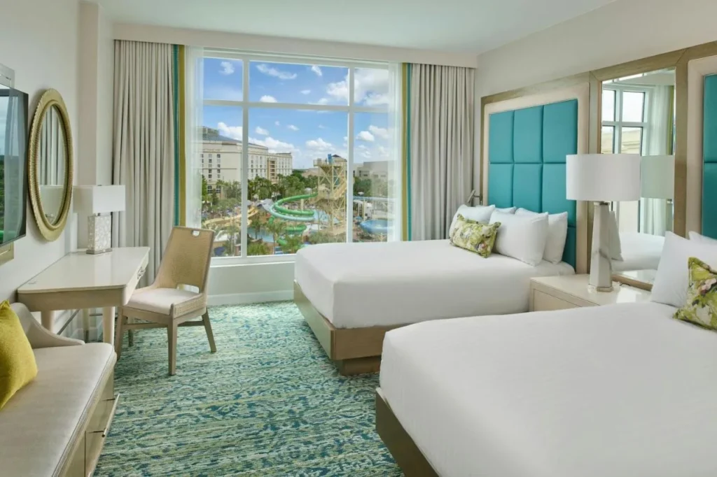 habitación con dos camas queen con cabeceras de color verde azulado y una ventana sobre el parque acuático en Gaylord Palms