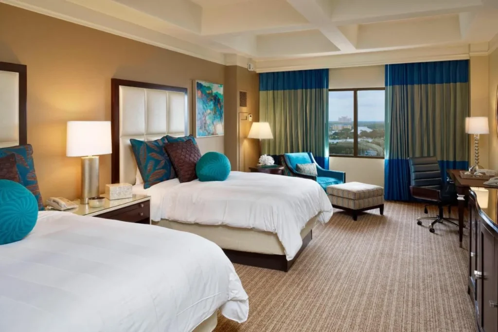 Two-queen room with teal pillows, blue curtains and a window at Renaissance Orlando at SeaWorld