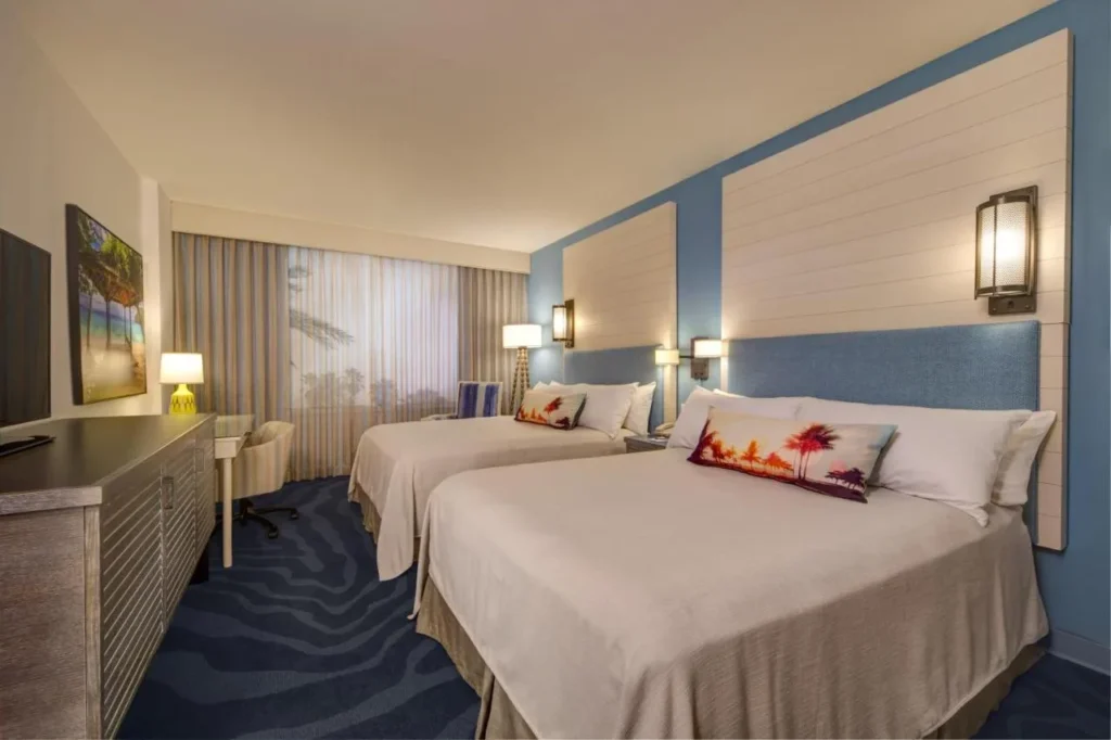 Habitación estándar de dos camas queen con pared de acento azul y almohadas con estampado de palma en Loews Sapphire Falls Resort