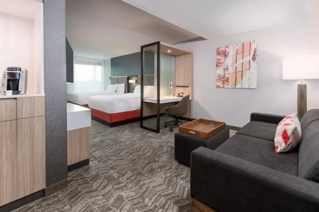 suite con dos camas queen en SpringHill Suites Lakeland con sofá, estación de café y escritorio con paredes de vidrio