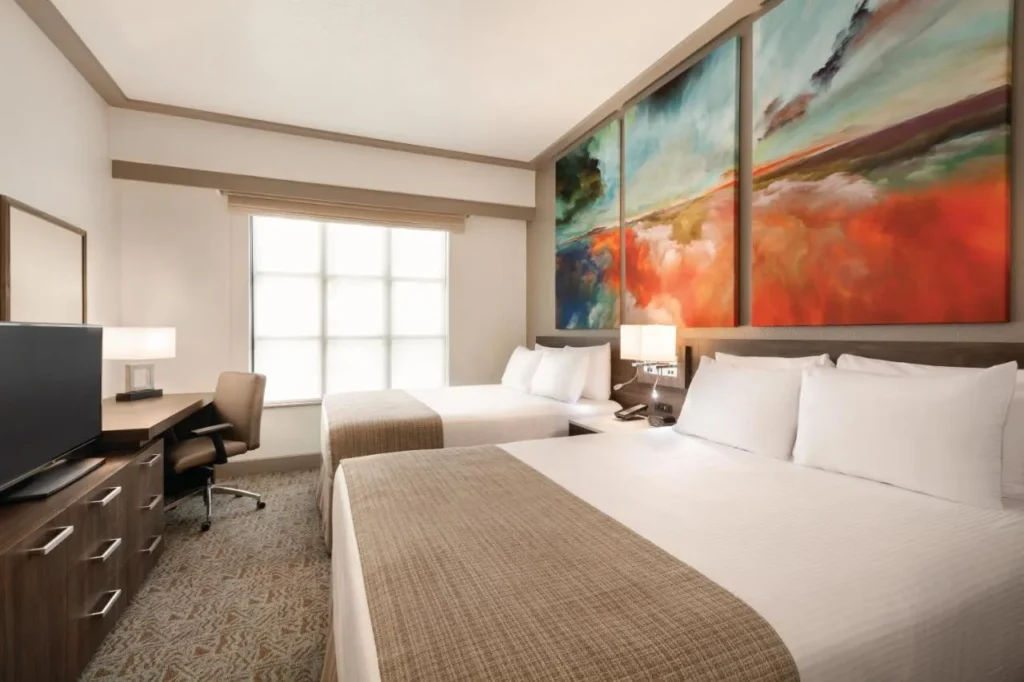 Two-queen suite bedroom with desk, TV and colorful abstract art at Buena Vista Suites
