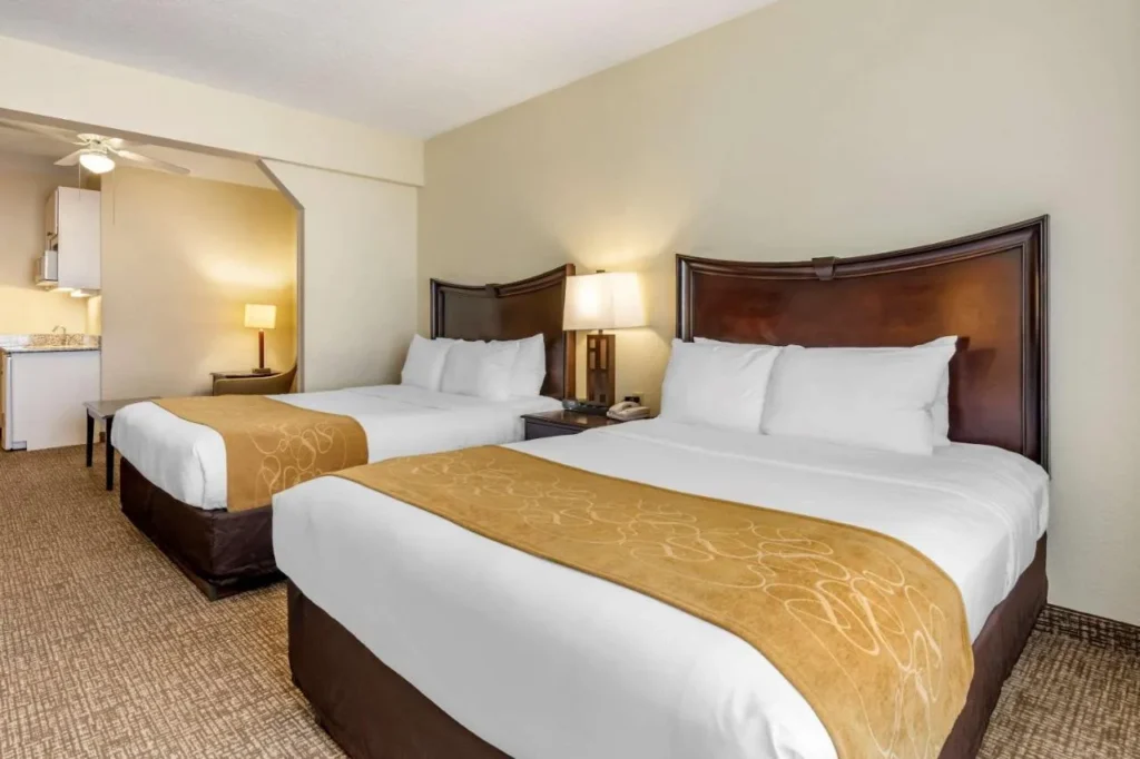 Two-queen suite with gold bed runners and kitchenette at Comfort Suites Maingate East