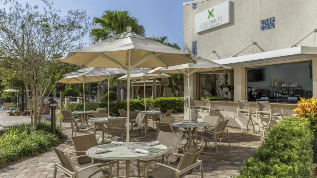 Mesas de patio sombreadas con sombrilla fuera del bar junto a la piscina Coconuts en Hyatt Regency Orlando