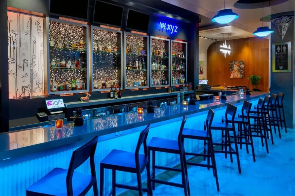 Bar W XYZ con mostrador iluminado en azul, taburetes altos y estantes para botellas en el Aloft Orlando Downtown