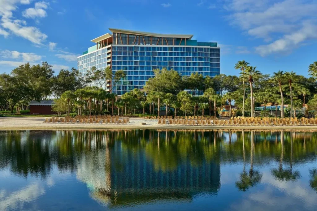 Torre Walt Disney World Swan Reserve reflejada en el lago detr&aacute;s de la playa y las palmeras