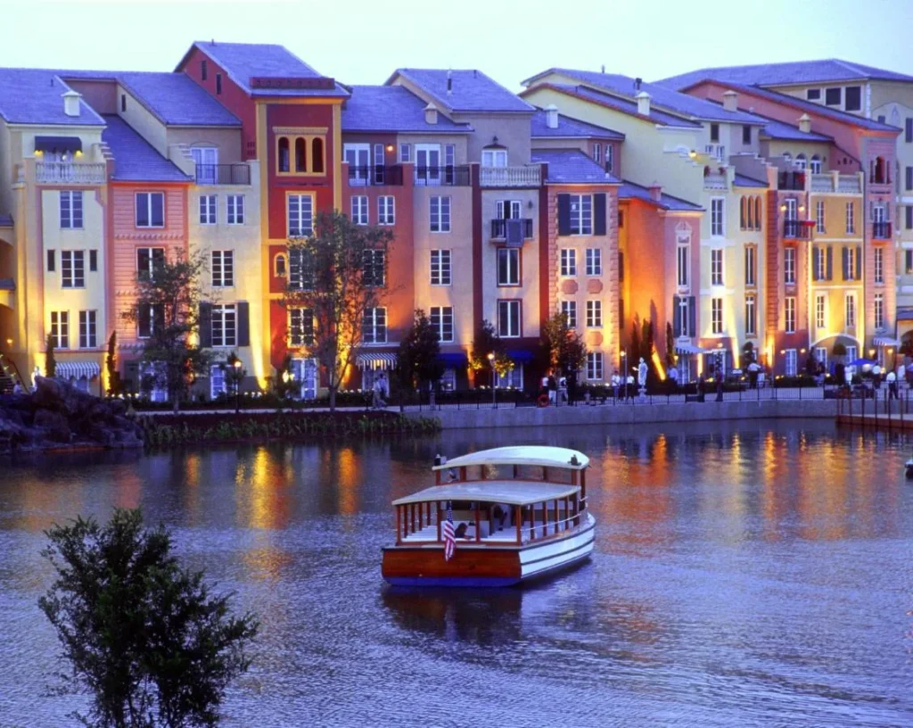 Water taxi crossing the harbor below lit, colorful facades at dusk, Loews Portofino Bay Hotel