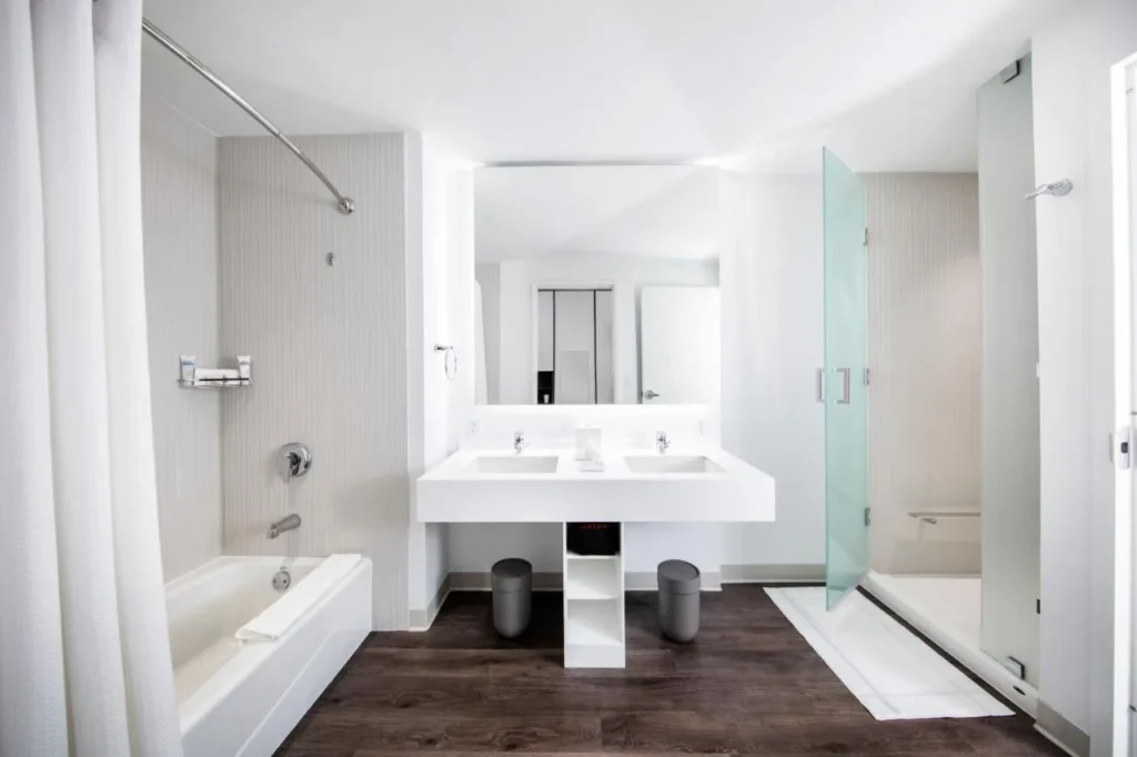 Cuarto de ba&ntilde;o blanco con lavabo doble, ba&ntilde;era y ducha de vidrio esmerilado en Universal Aventura Hotel