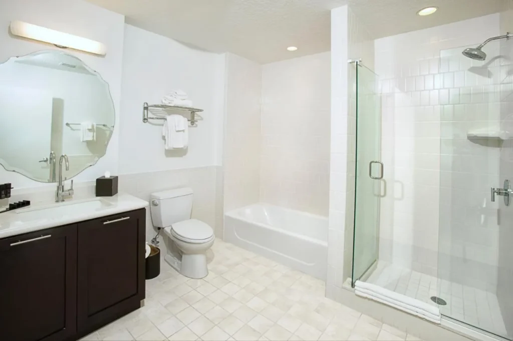 Baño blanco con bañera, ducha de cristal y tocador oscuro en Meliá Orlando Celebration
