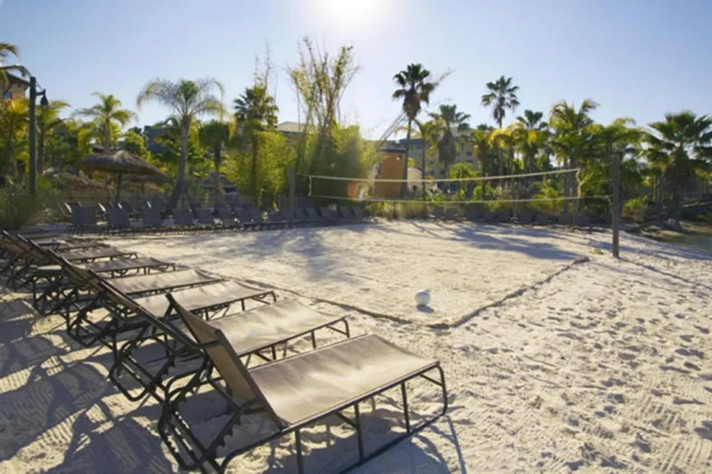 Playa de arena blanca con tumbonas y una red de voleibol en Loews Royal Pacific Resort