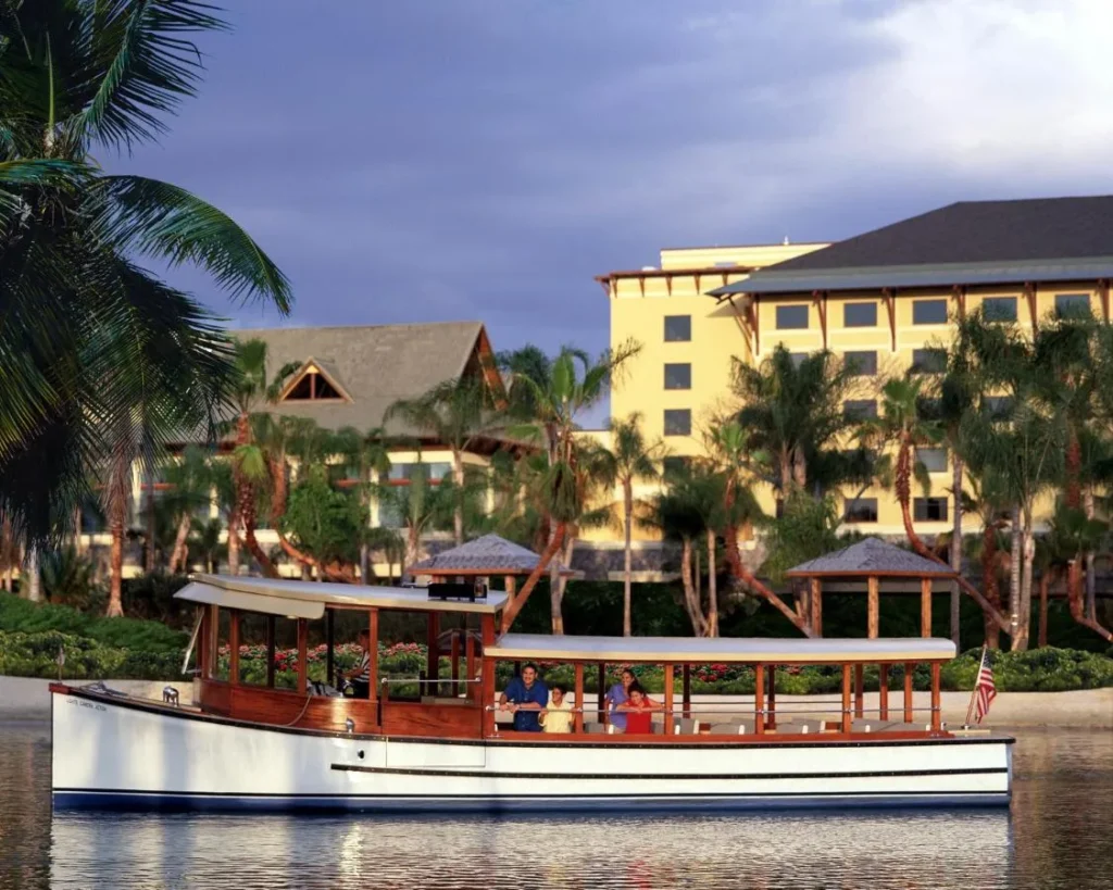 Wooden water taxi with passengers cruising past palm trees at Loews Royal Pacific Resort