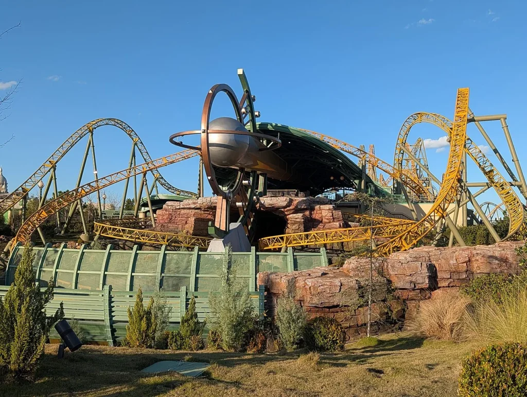 Yellow and green Stardust Racers coaster tracks loop around a ringed sphere sculpture, Epic Universe