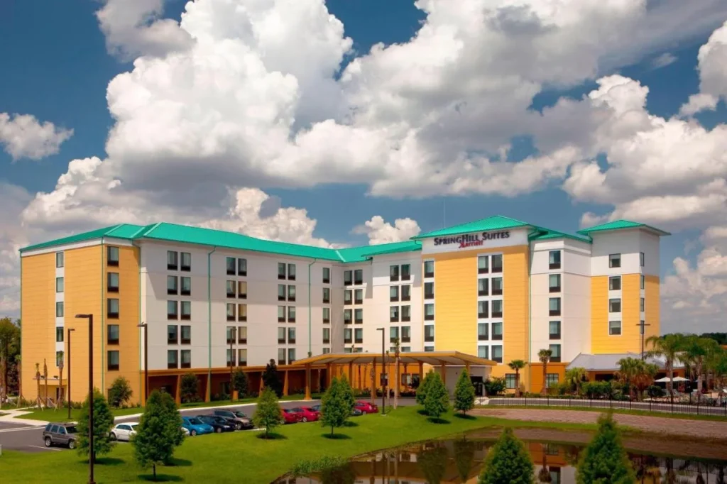 Exterior amarillo y blanco junto a un estanque en SpringHill Suites Orlando at SeaWorld bajo las nubes de verano