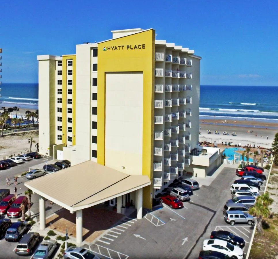 Yellow and white tower of Hyatt Place Daytona Beach-Oceanfront with its parking lot, pool and beach