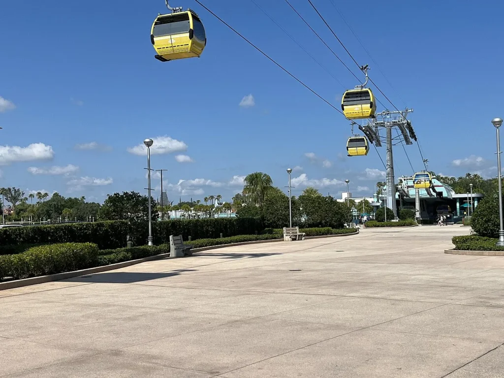 Yellow Disney Skyliner gondolas above the walkway near the Hollywood Studios station and entrance plaza