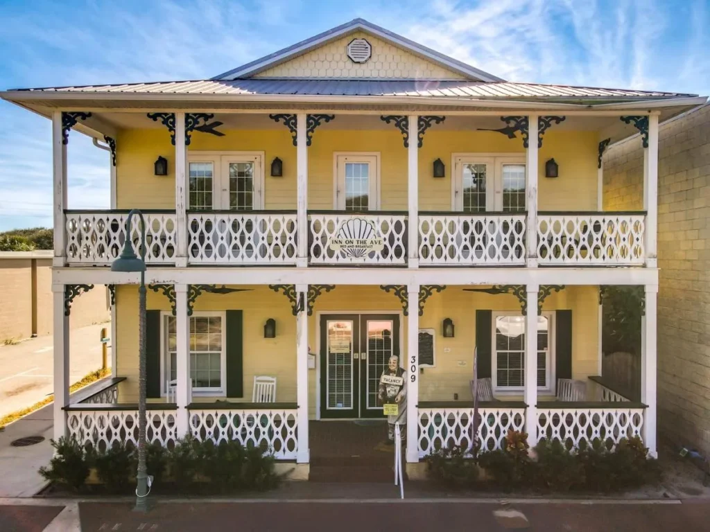 Yellow two-story bed and breakfast with white porch railings at Inn on the Avenue, New Smyrna Beach